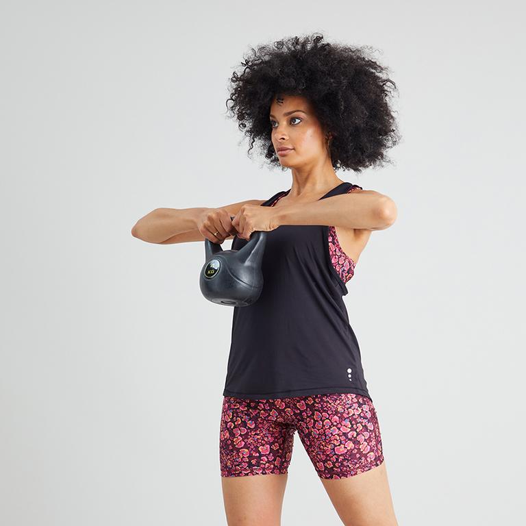 A woman in a black double layer vest top holding a kettlebell.