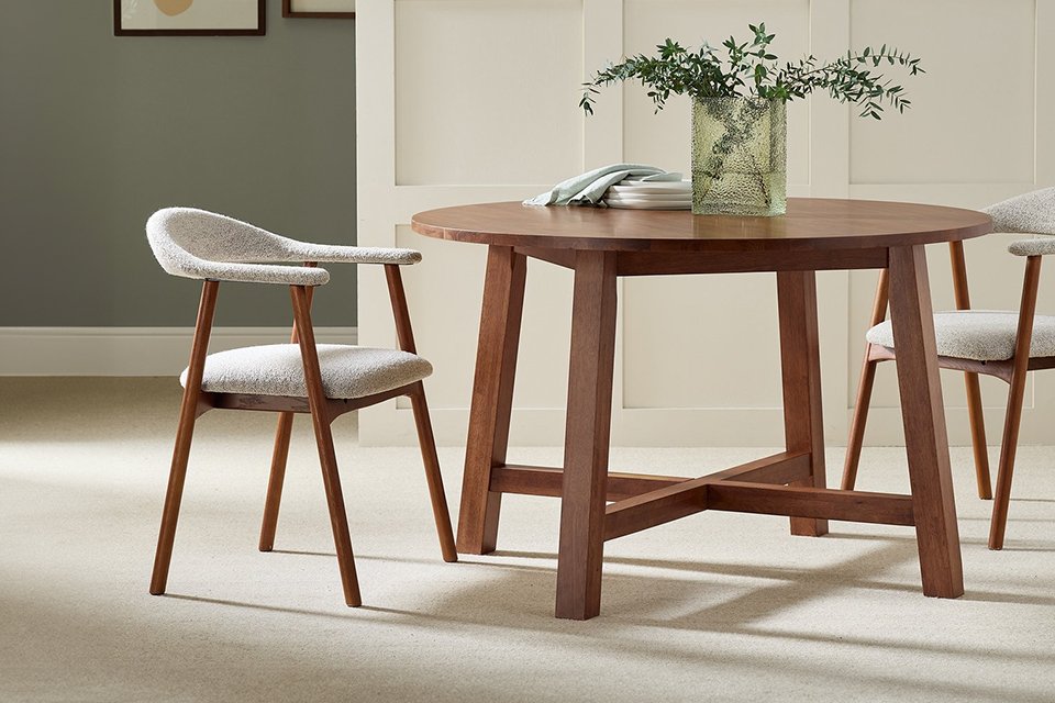 Dark circle wooden dining table with green plant on top and green walls.