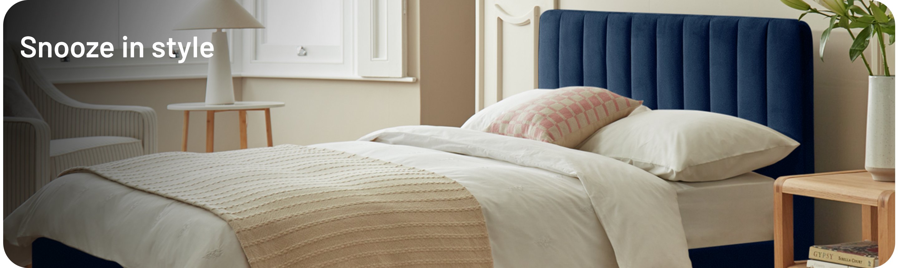 Throw, pillows and blanket neatly layered over a dark ink blue ottoman bed in a bedroom.