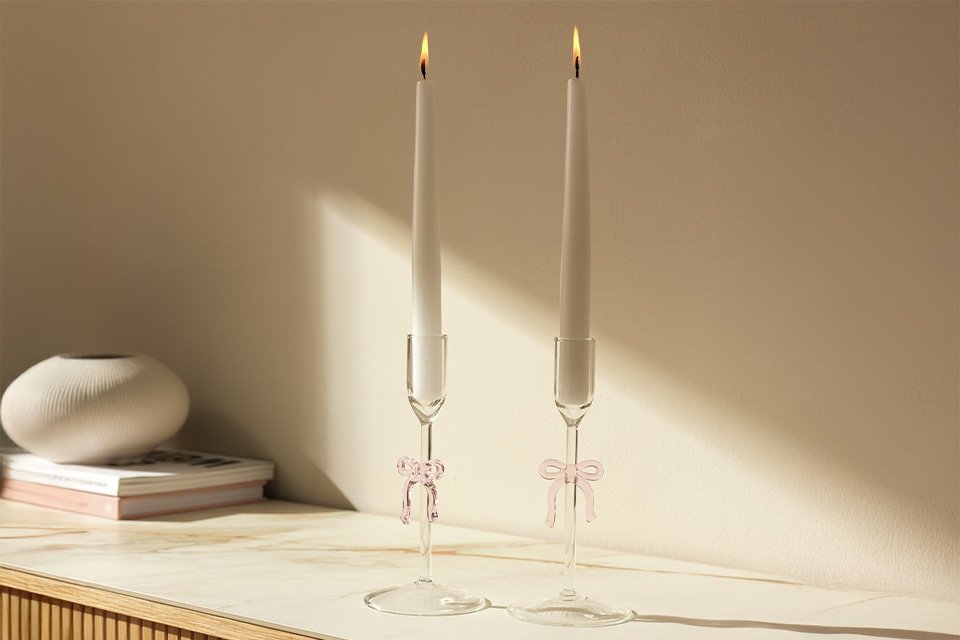 Clear glass candle sticks with pink bows on wooden sideboard.