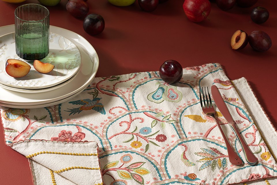 Habitat x Natonal Trust place mats layered with one in a floral pattern and one in a striped mustard colour pattern with plates set on a dining table ready for hosting a meal.