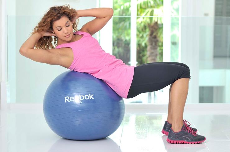 A woman working out at home using a gym ball.