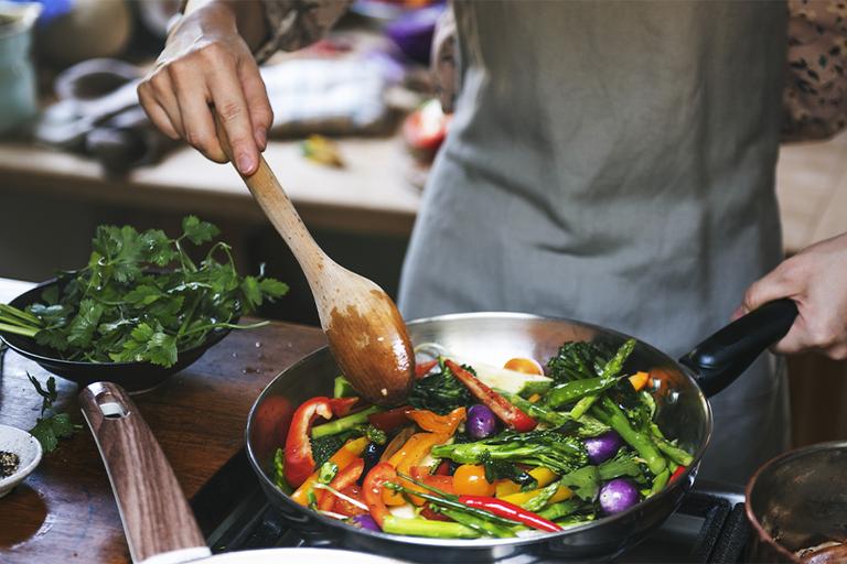 A person stirring a frying pan full of healthy vegetables