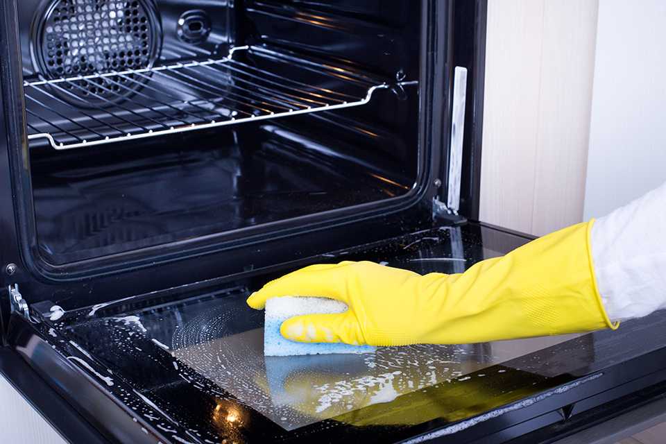 A person in yellow gloves cleaning the oven.