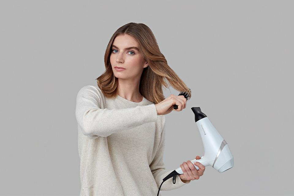 A woman blow drying her hair, using a hair brush to style.