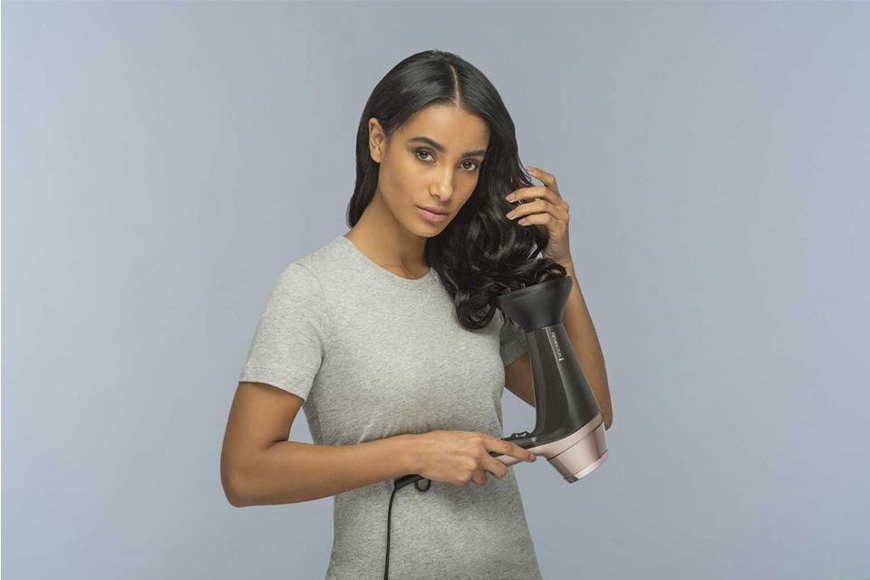 A lady using the diffuser attachment on her hair dryer to dry her wavy hair.