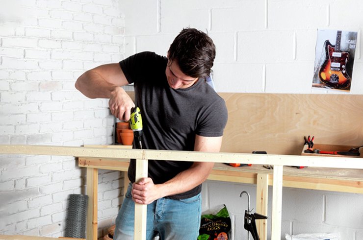 A man using a cordless electric screw driver on a wooden frame