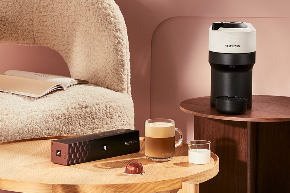 A Nespresso Vertuo Pop coffee machine on a table with other things in a living room setup. 