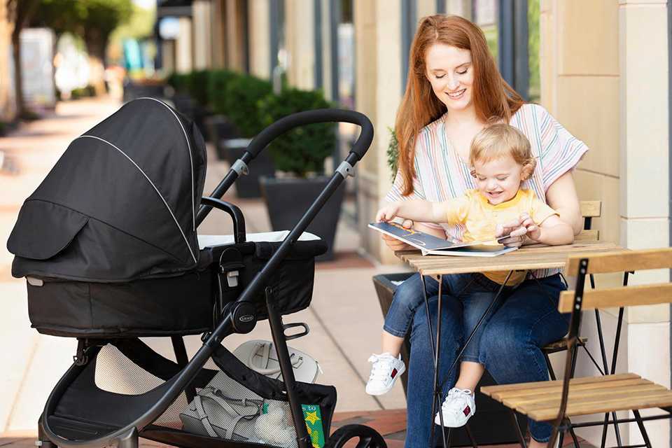 A baby sitting on a mother's lap near a pushchair.