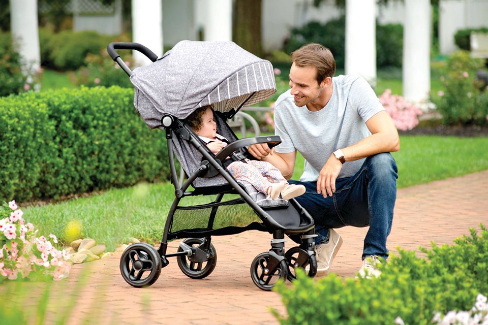 A man playing with his baby sitting in a pushchair outdoors.