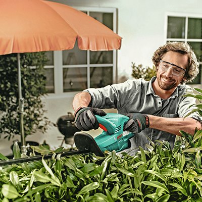 A man using a hedge trimmer to cut hedges.