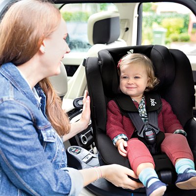 A mother looking at her baby in a car seat.