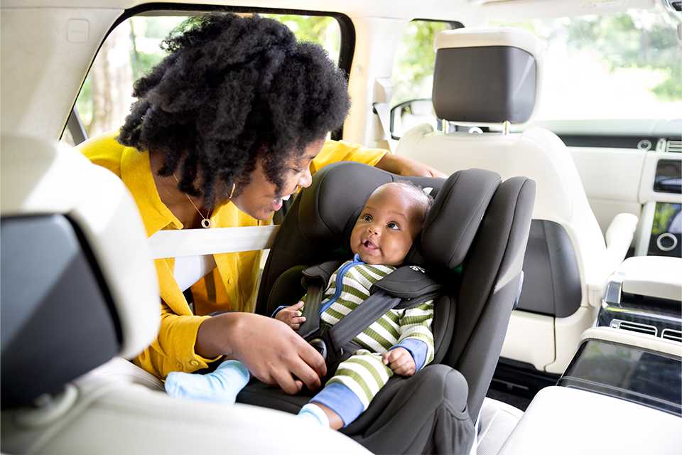 A mother ensuring her baby is fastened well in the Joie every stage™ R129 car seat.
