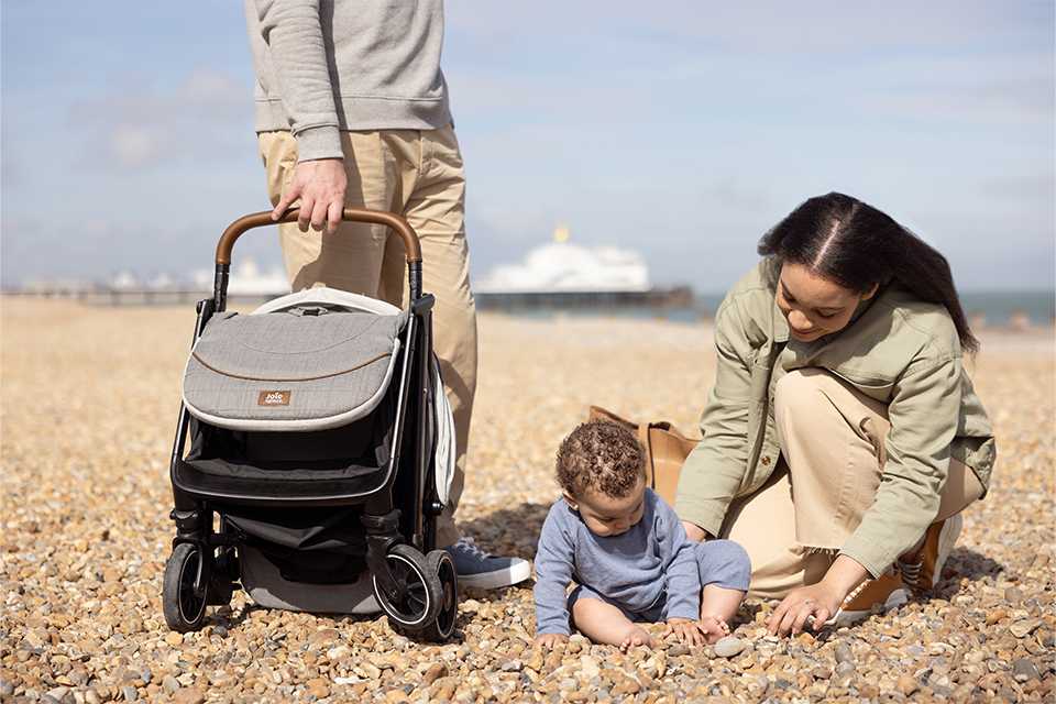 : Family on the beach with their Joie parcel™ stroller and baby.