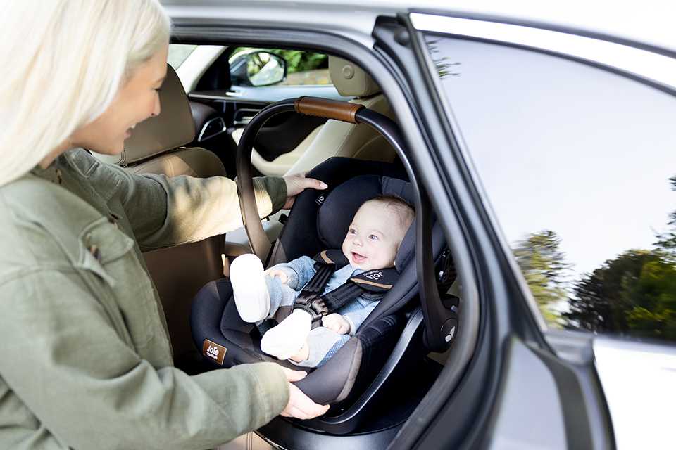 A mother putting her baby in a Joie i-Level™ recline infant carrier into the car. 