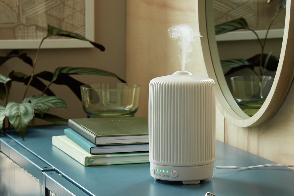 A white electric diffuser near a mirror and some books on a sideboard.