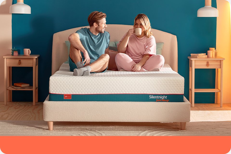 A couple chatting and having some tea while sitting on a Silentnight Just Sleep mattress.