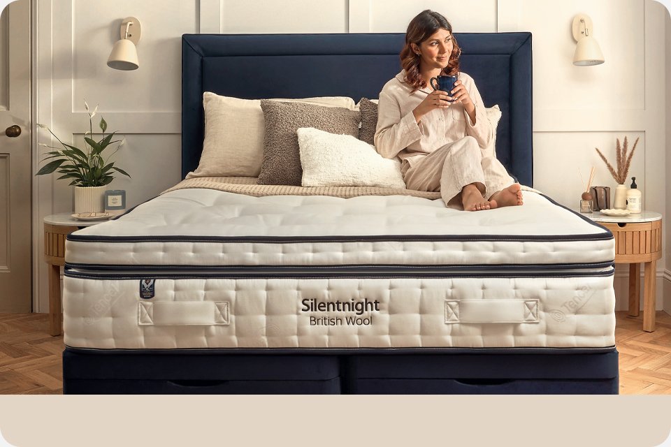 A woman sitting on a Silentnight British wool mattress and enjoying a cup of tea.