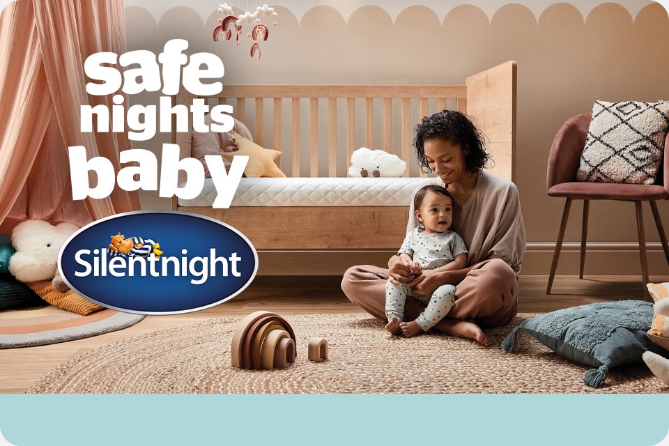 Mum cuddling her baby while sitting in front of a cot with Silentnight cot bed mattress.