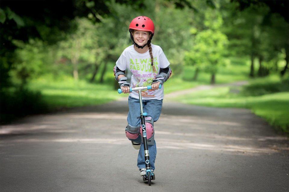 A girl riding a EVO Light Blast Foldable 2 Wheel Scooter - Blue.