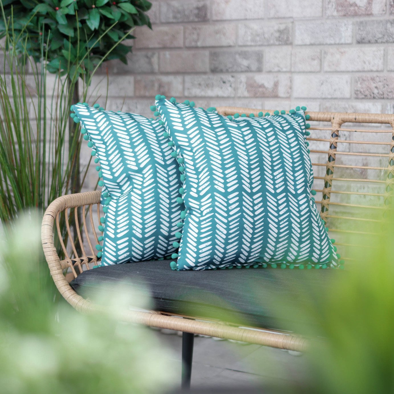 two teal cushions on a rattan effect garden sofa