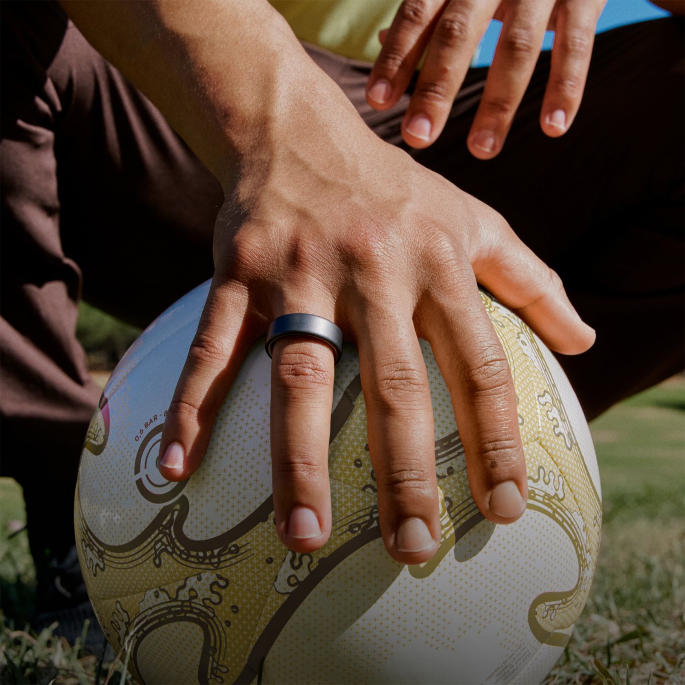 Space grey colour Oura Ring 4 on a hand resting on top of a football