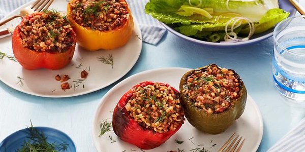 Table laid with 2 plates of stuffed bell peppers with a side salad.
