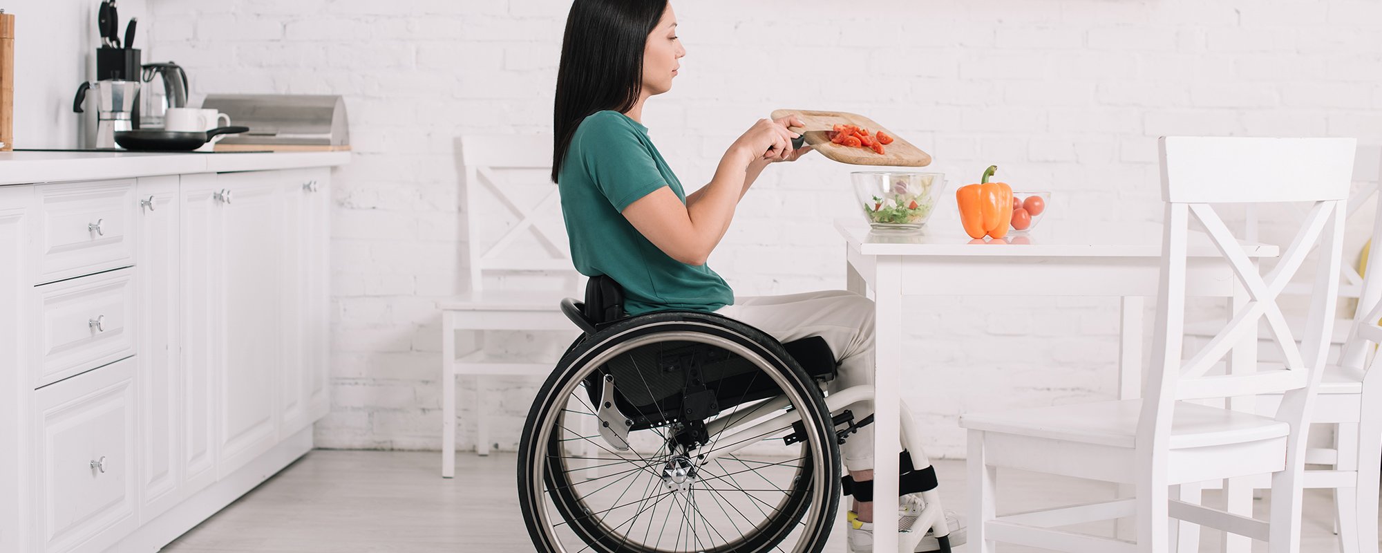  A woman in a wheelchair chopping vegetables in her kitchen.