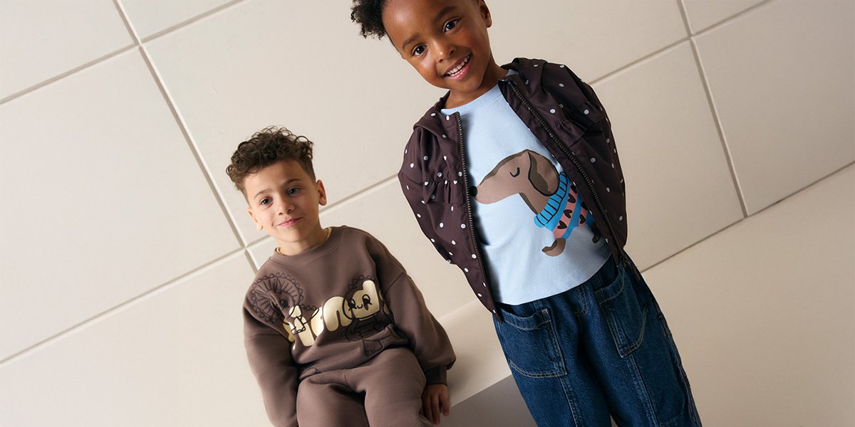 Boy wearing brown co ord set and girl wearing brown and blue polka dot jacket with sausage dog blue t-shirt and jeans.