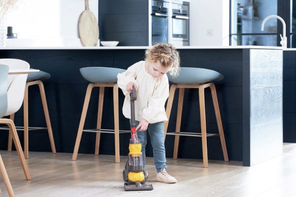 A girl in a kitchen with a toy hoover.