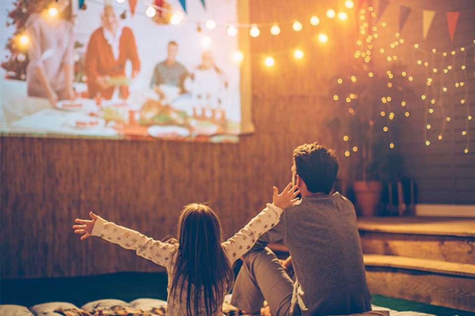 A father and a daughter enjoying a movie night at home, projected on the big garden wall.