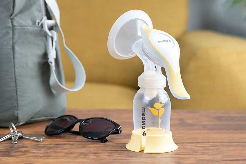 Medela Harmony manual breast pump in yellow colour placed on a wooden table next to a bag. 