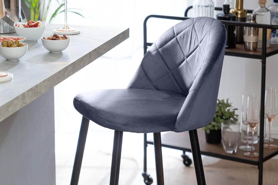 A quilted fabric bar stool in grey placed next to a breakfast counter.