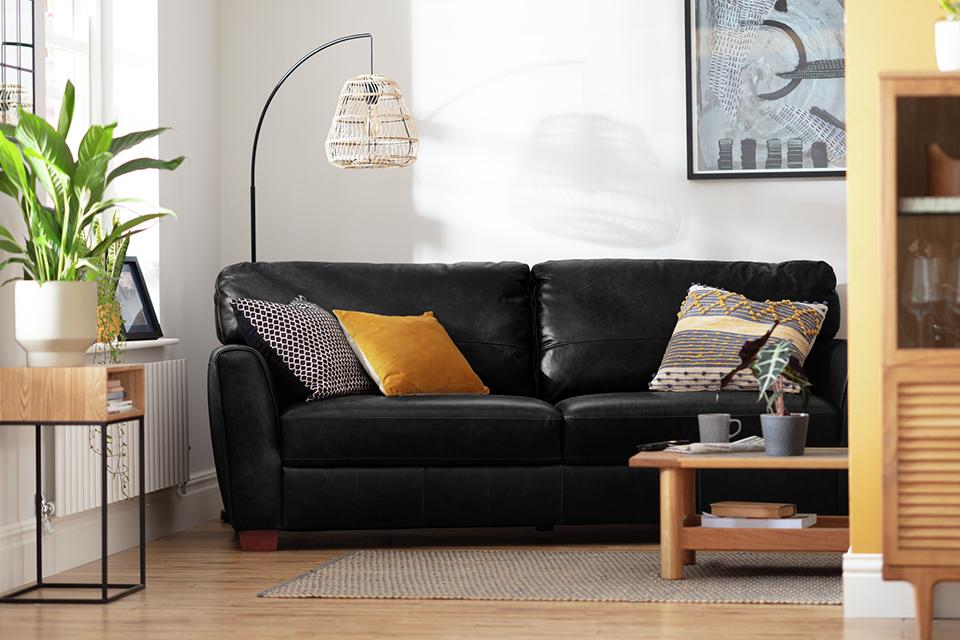 A Habitat 4 seater black leather sofa placed in a living room in front of a wooden coffee table. 
