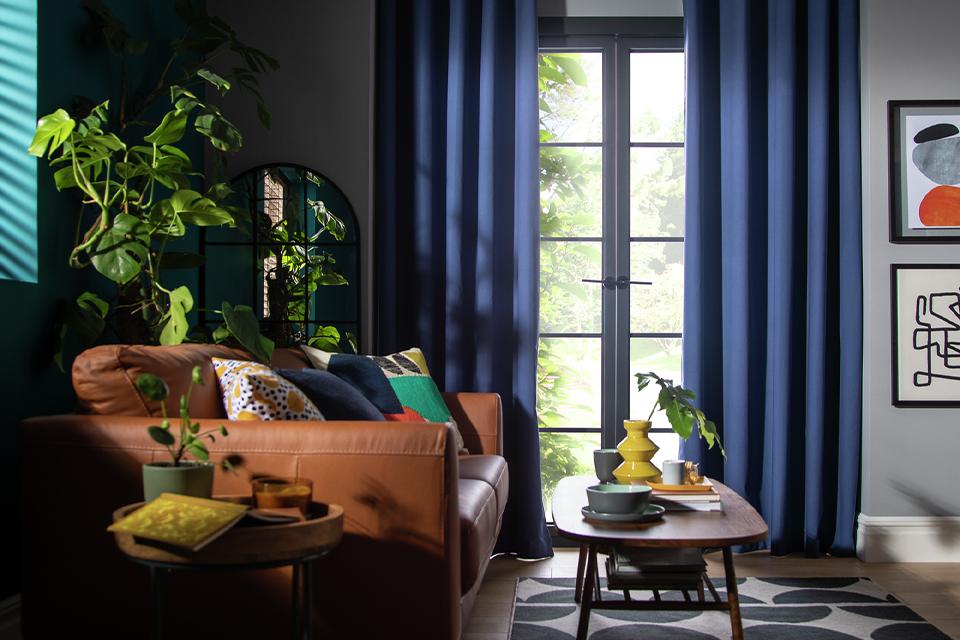 A Habitat plain navy blue blackout eyelet curtain in a living room with brown sofa and wooden coffee table.