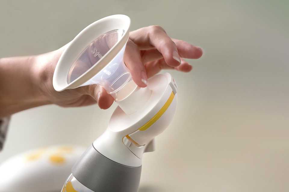 A close up image of a woman holding an electric breast pump in grey and yellow.