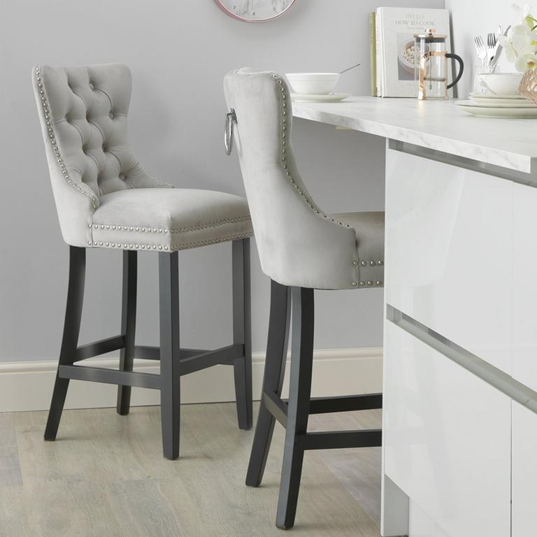 A grey velvet bar stool with black legs next to a white table.