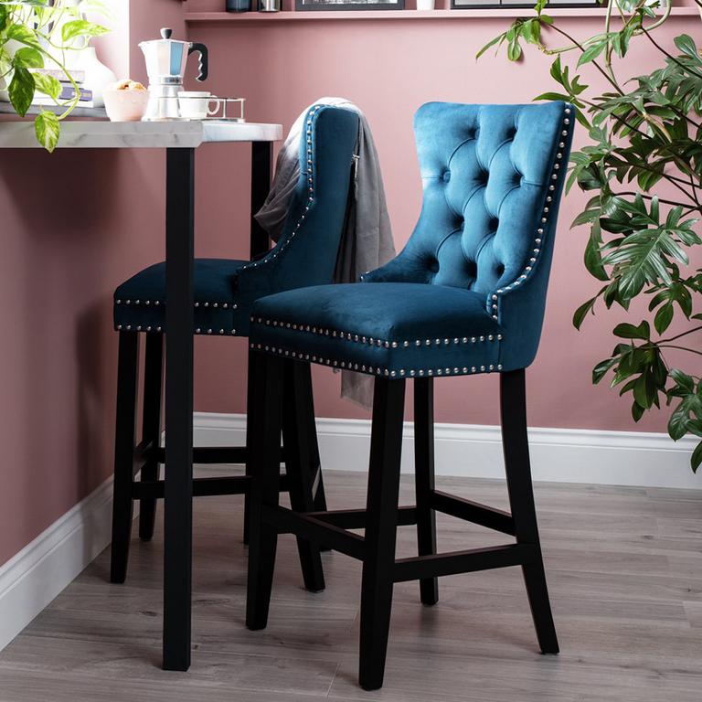 A blue velvet buttoned bar stool in a pink room.