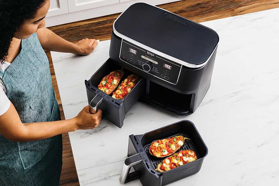 A woman cooking food in a black Ninja air fryer with 2 drawers.