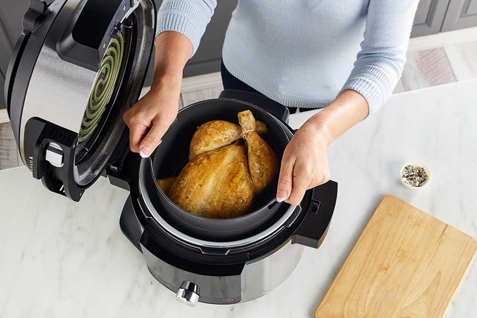 A user in a white long-sleeve top placing a whole turkey inside a Ninja multi-cooker.
