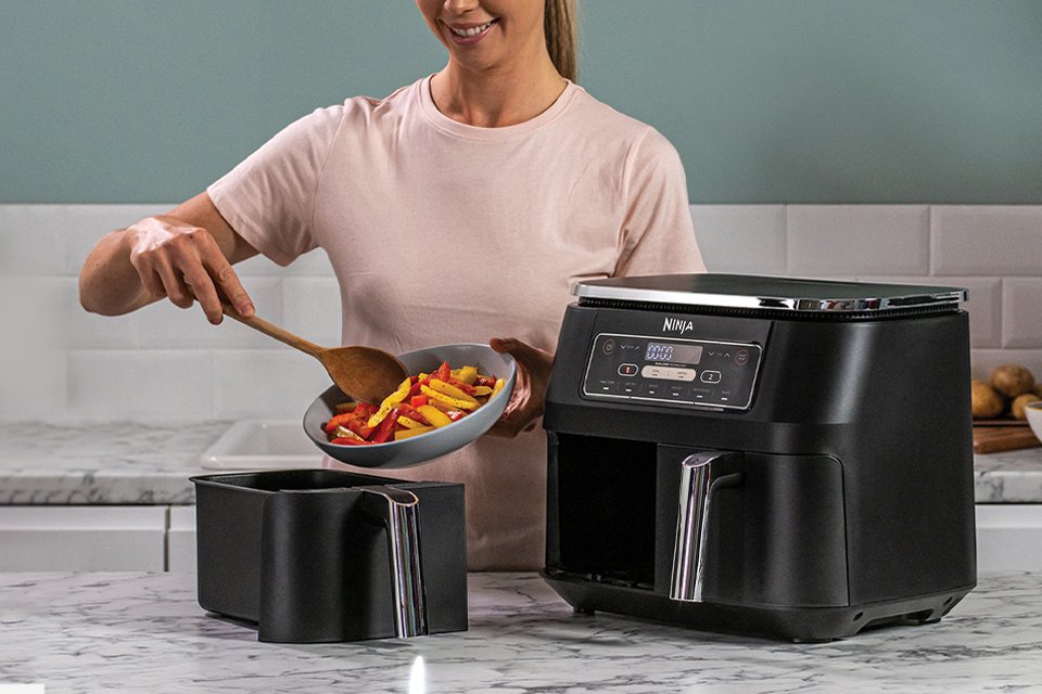 A woman cooking vegetables in a Ninja air fryer and dehydrator.