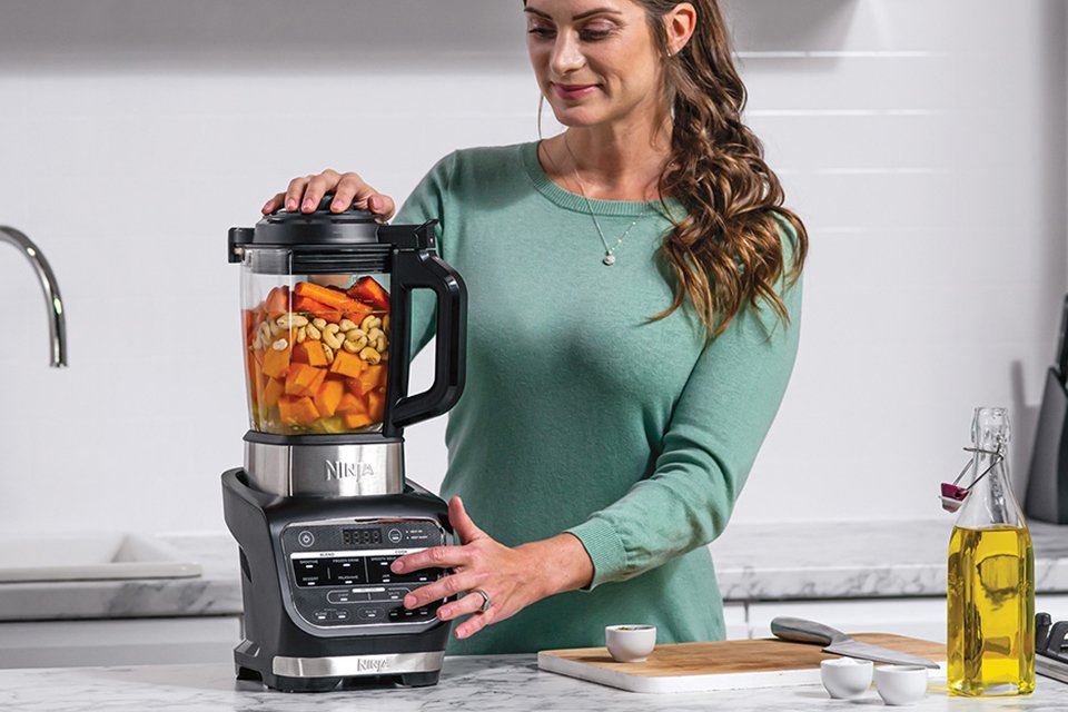A woman blending chopped vegetables and fruits in a Ninja blender and soup maker.