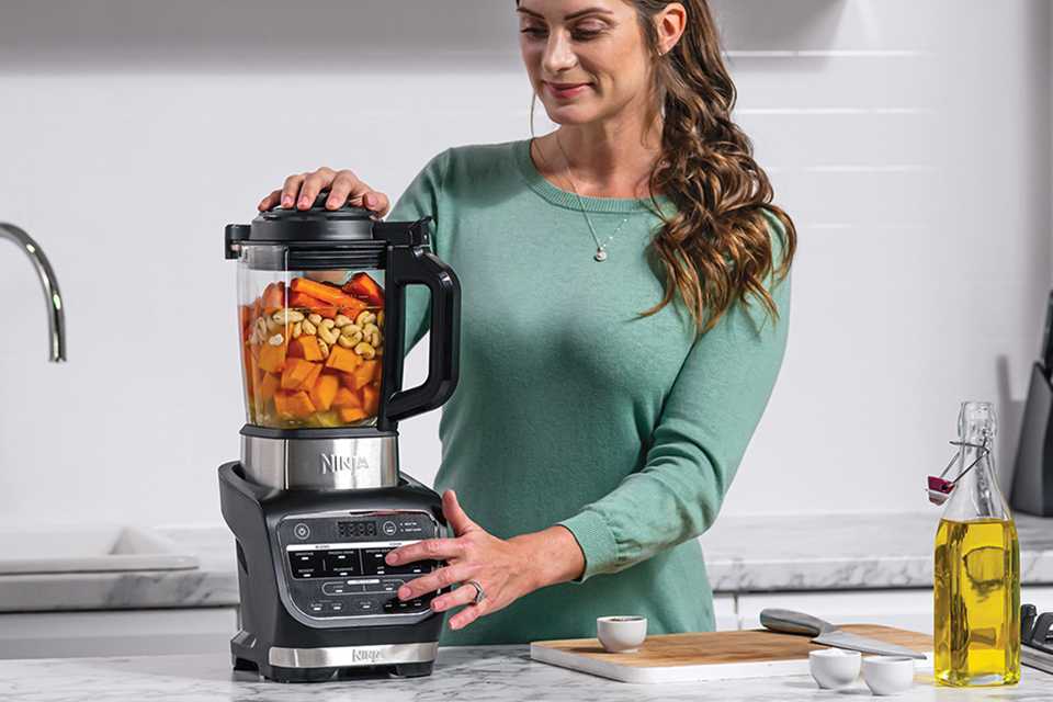 A woman blending chopped vegetables and fruits in a Ninja blender and soup maker.