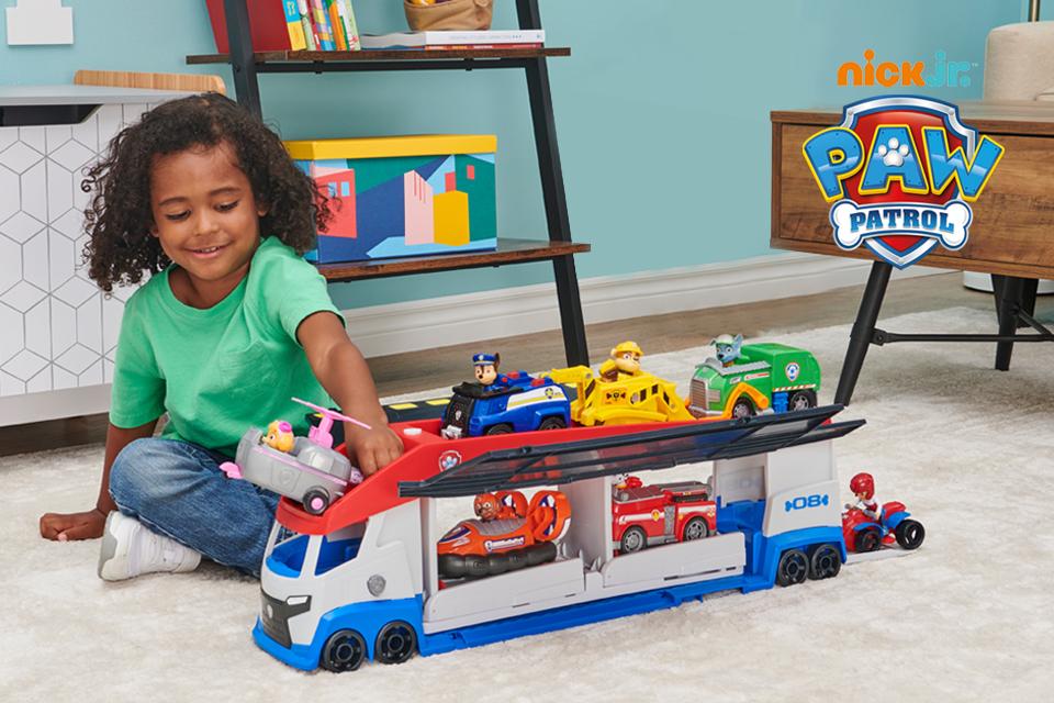 A child playing with a PAW Patroller truck, transformer vehicles and playsets, with the Nick Junior PAW Patrol logo on top.