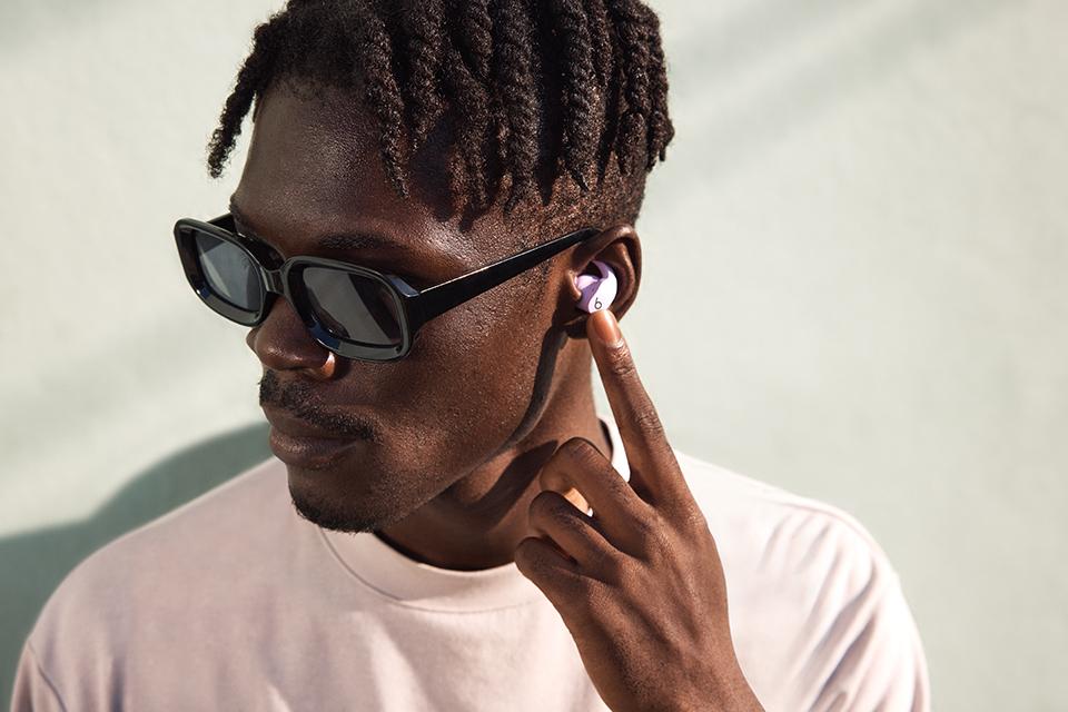 A man in a white t-shirt and black sunglasses wearing a pair of white Beats Fit Pro earbuds.