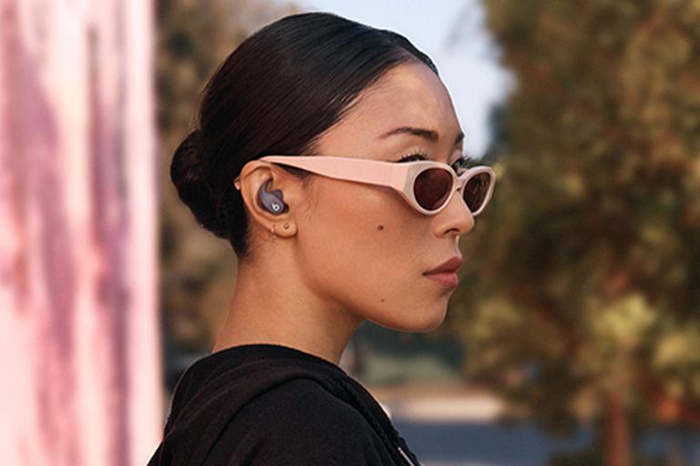 A woman in a black hoodie with sunglasses wearing a pair of grey Beats Fit Pro wireless earbuds.
