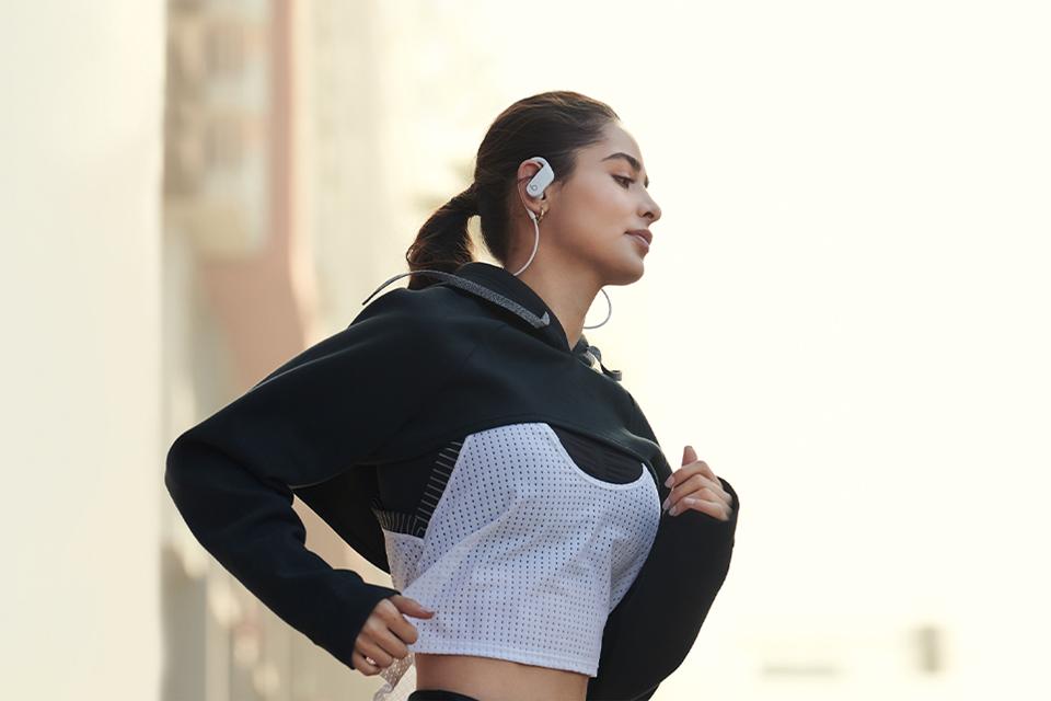A woman in a black and grey tracksuit top wearing a pair of white Beats Powerbeats earphones while running.