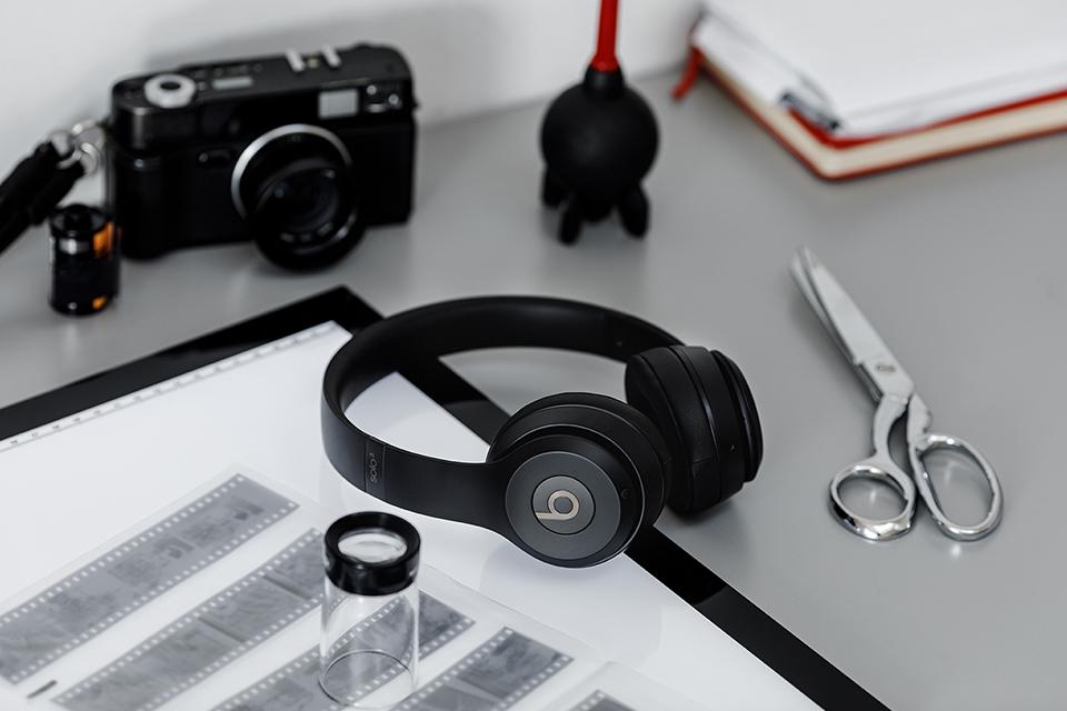 A pair of black Beats Solo 3 headphones with a camera, negative films, a dust blower, and a scissor on a table.