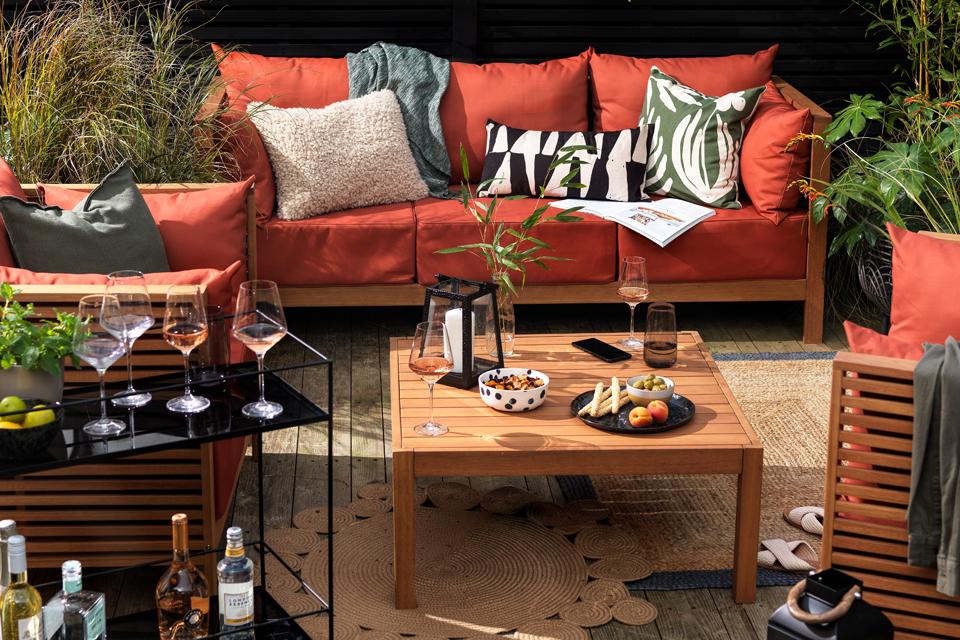 A garden party set up with coral garden sofa set and wooden table holding drinks and nibbles.