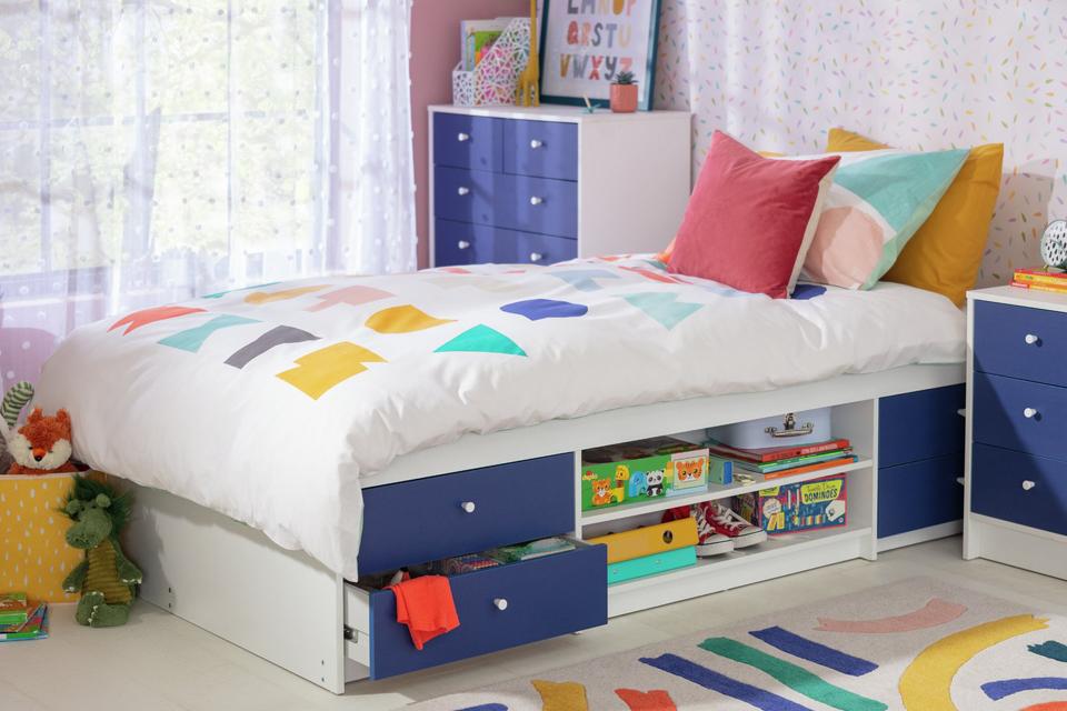 A blue and white kid's cabin bed with multi-coloured bedding.